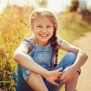 girl sitting on dirt road smiling